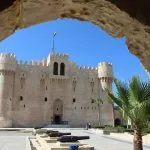 The historic Alexandria Qaitbay Citadel seen through an archway, with cannons in the foreground.
