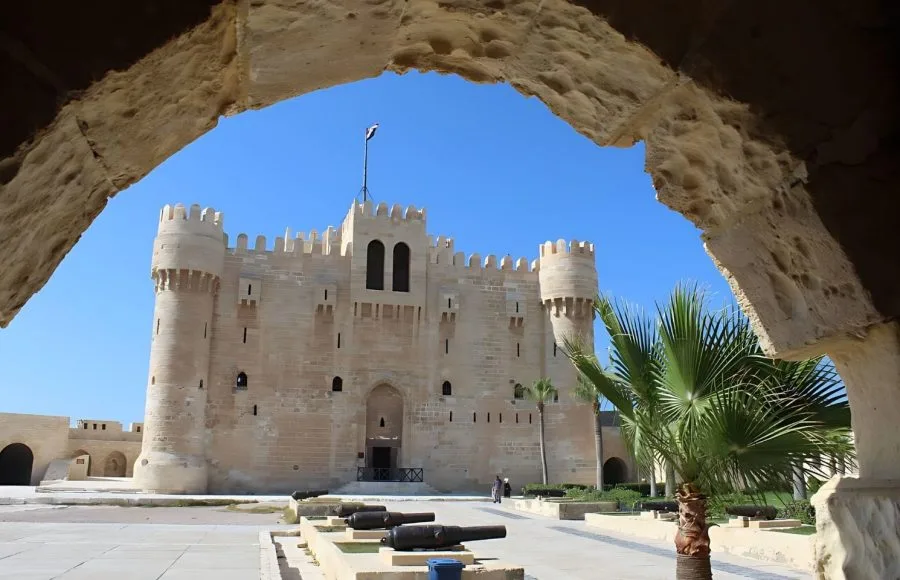 The historic Alexandria Qaitbay Citadel seen through an archway, with cannons in the foreground.