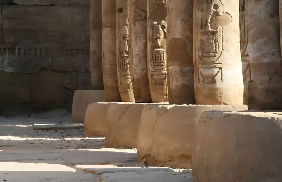 A low-angle shot of a row of thick, weathered Ancient Columns Of The Temple In Abydos, showing hieroglyphs carved into the sandstone surfaces.