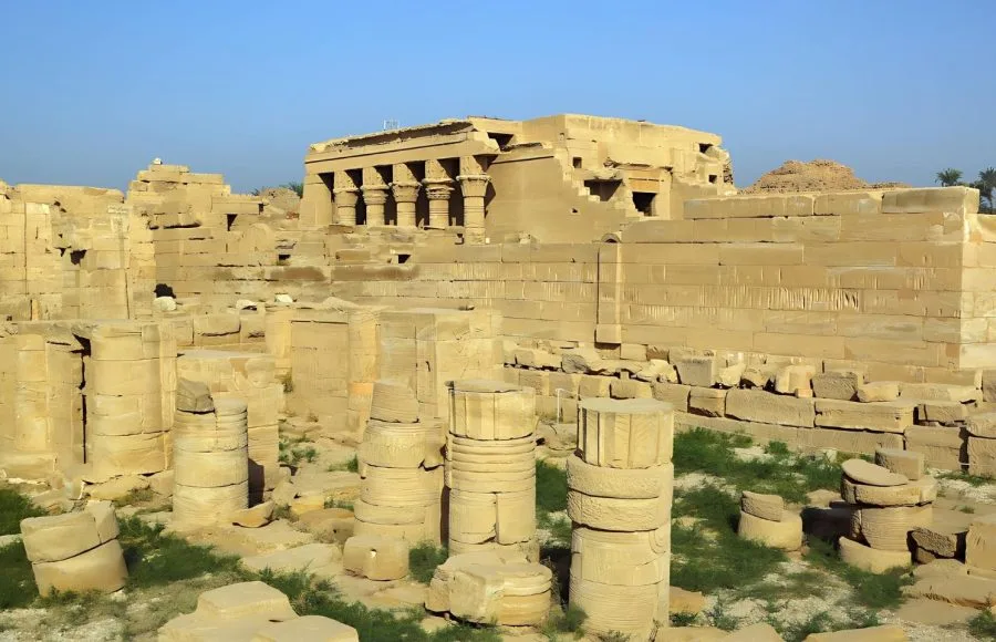 The sun-drenched ruins of the Ancient Egyptian Temple At Dendera, showing fallen columns and the main structure in the background.