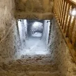 Steep, narrow stone staircase with wooden handrails descending into an unfinished, rough-cut chamber in an Amarna tomb.