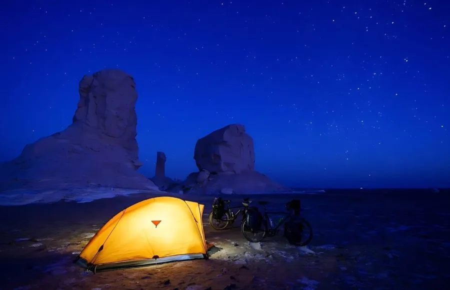 Illuminated tent and bicycles under a starry night sky in the White Desert, Egypt.