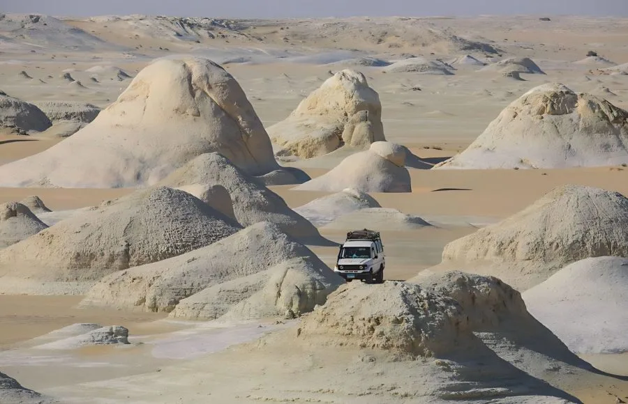White 4x4 car driving among beautiful, pale sand formations in the White Desert, Egypt.