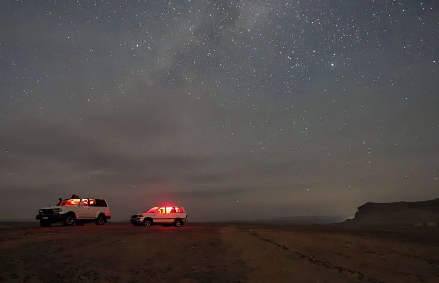 Two cars with interior lights on, parked under a dark, starry sky in the Wadi El Rayan desert in Fayoum.