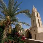 Palm tree and bell tower of the Church of St. Bishoy Monastery, set against a bright blue sky in Wadi El Natrun.