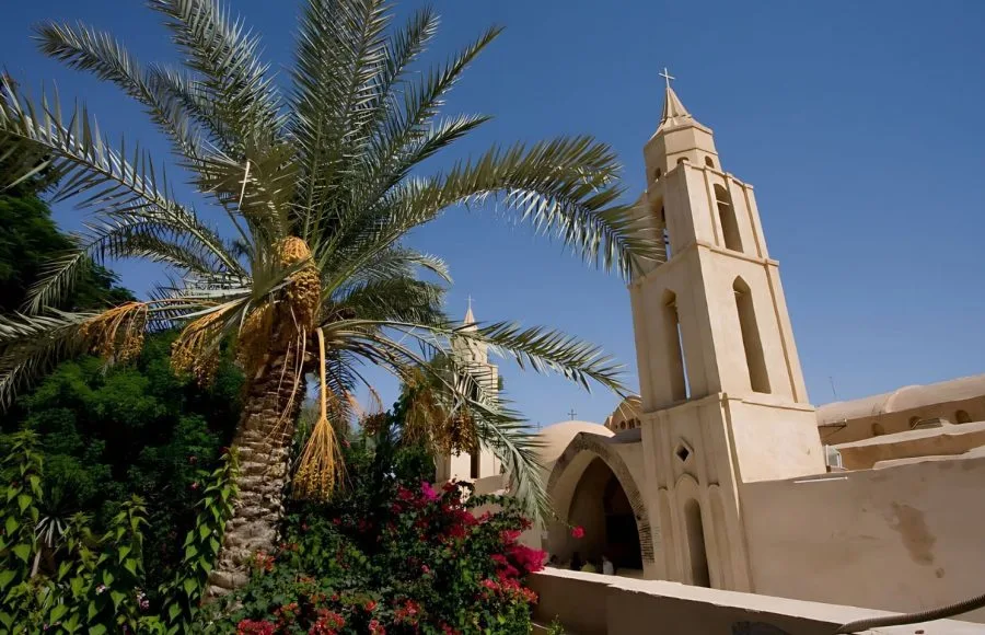 Palm tree and bell tower of the Church of St. Bishoy Monastery, set against a bright blue sky in Wadi El Natrun.