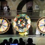 Blurred motion of three Tanoura dancers spinning large geometric patterned skirts.
