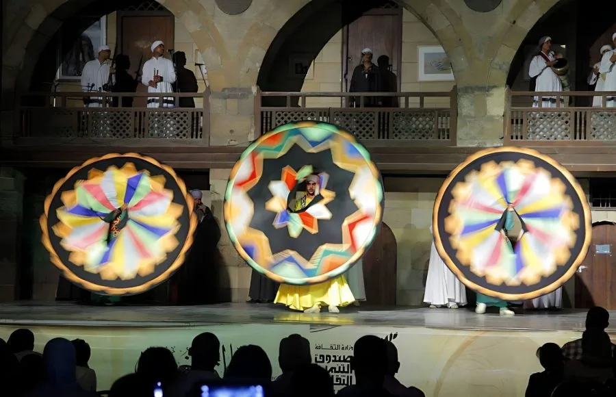 Blurred motion of three Tanoura dancers spinning large geometric patterned skirts.
