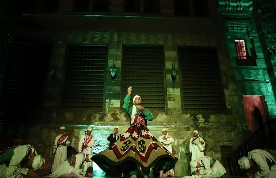 A Sufi dancer looking upward under atmospheric green lights at Wekalet El Ghouri.