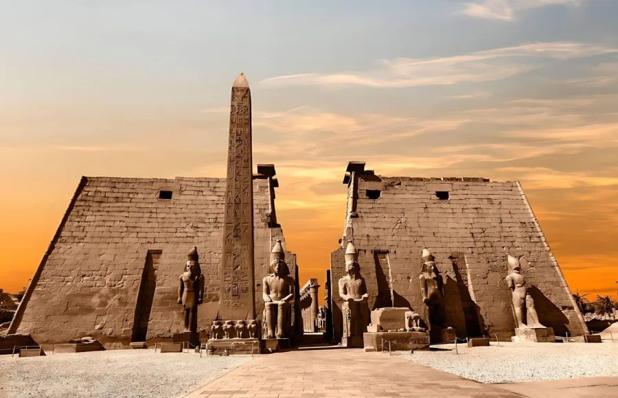 A beautiful sunset casts a warm glow on the towering obelisk and statues at the entrance of the Luxor Temple