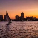 A traditional Egyptian felucca sailing on the Nile against a vibrant purple and orange sky.