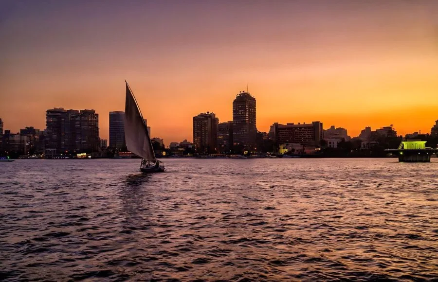A traditional Egyptian felucca sailing on the Nile against a vibrant purple and orange sky.