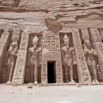 The colossal rock-cut statues at the Exterior Entrance To Ancient Egyptian Temple Of Queen Nefertari In Abu Simbel, showing the facade carved into the cliff face.