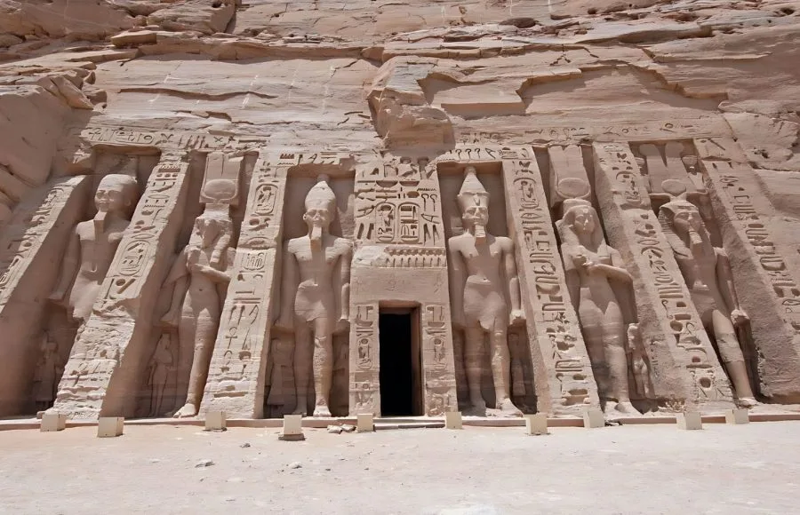 The colossal rock-cut statues at the Exterior Entrance To Ancient Egyptian Temple Of Queen Nefertari In Abu Simbel, showing the facade carved into the cliff face.