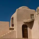 Close-up of the sunlit, geometric mud-brick architecture and staircase of the Coptic Monastery of Al-Baramous against a deep blue sky in Wadi El Natrun.