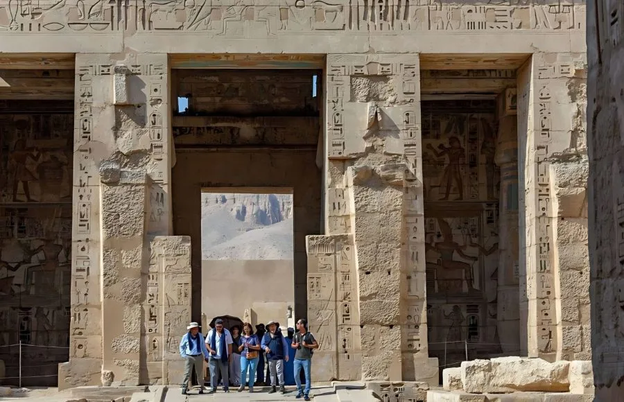 Tourists standing beneath the monumental Gateway at the Mortuary Temple of Ramesses III Medinet Habu, highlighting the massive stone entrance covered with detailed hieroglyphs and pharaonic reliefs.