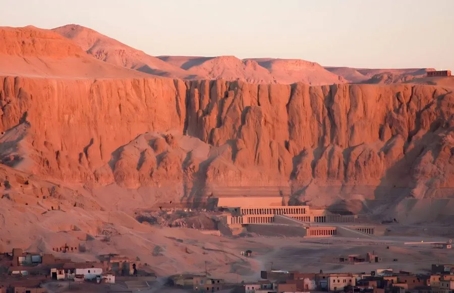 Hatshepsut's temple at Deir el-Bahari against the Theban cliffs at sunset.