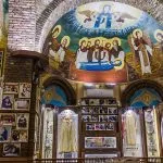 Richly decorated interior of a chapel at Saint Pishoy Monastery featuring frescos, icons, and displays of vestments.
