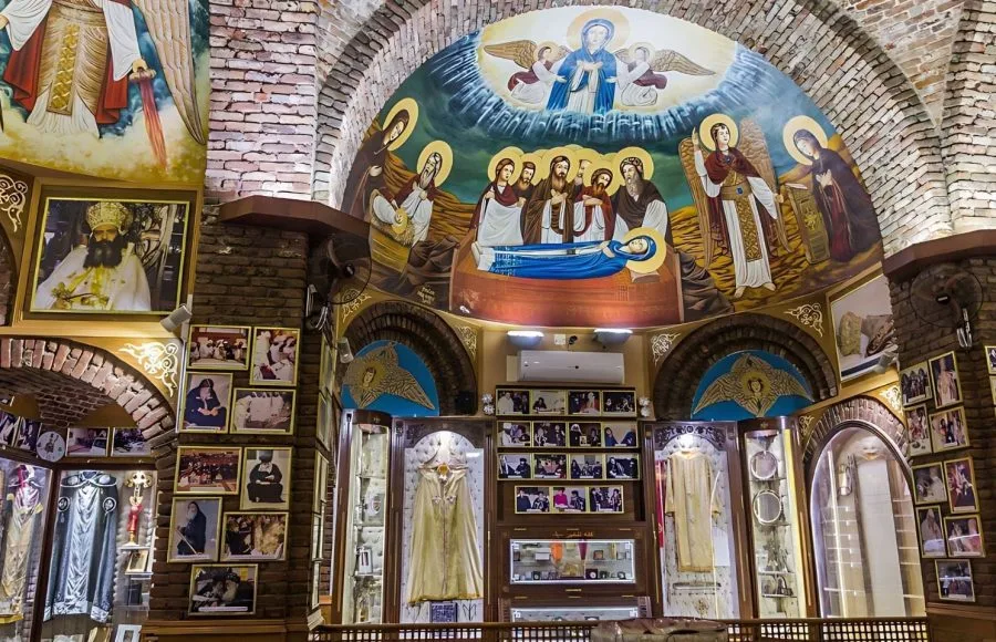 Richly decorated interior of a chapel at Saint Pishoy Monastery featuring frescos, icons, and displays of vestments.