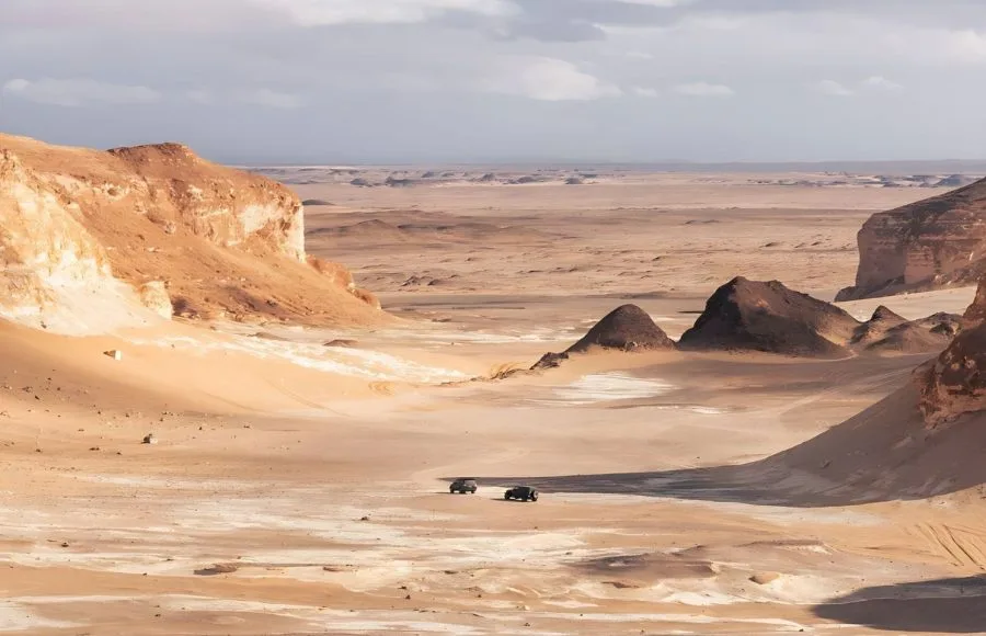 Two jeeps driving through the wide, rugged landscape of the Valley of Agabat in the Egyptian desert.