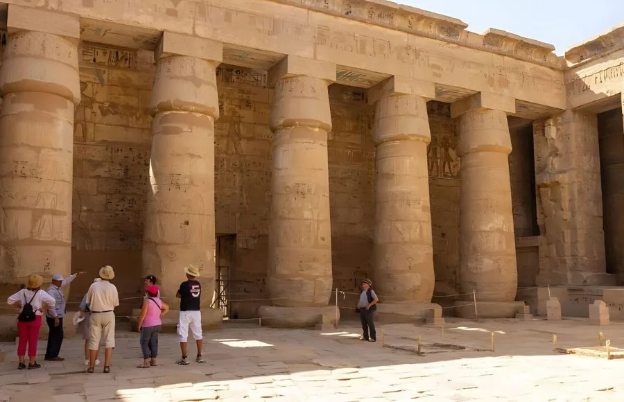 Tourists walking beneath the Large columns in the Medinet Habu temple, showing the massive, undecorated stone pillars of the peristyle court in the Mortuary Temple of Ramesses III.