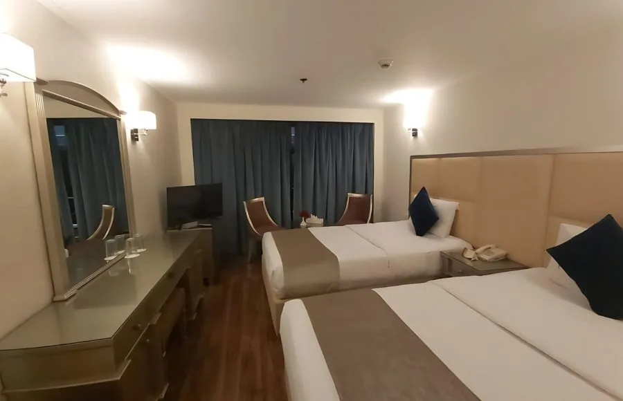 Twin-bed cruise ship cabin with a dressing table and viewing window.