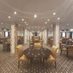 Cruise ship dining room with rows of tables and yellow upholstered chairs.