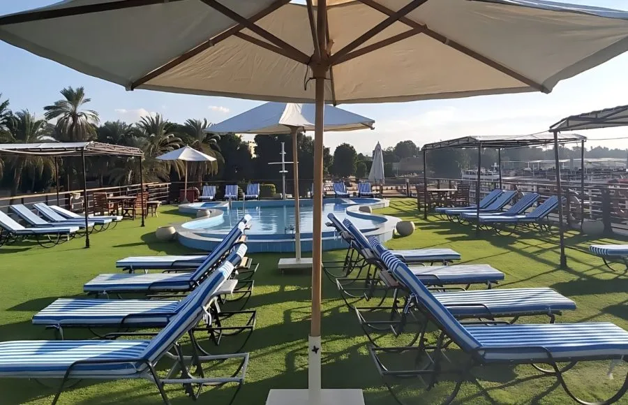 Cruise ship sundeck with blue striped loungers and a small pool under umbrellas.