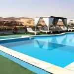 Cruise ship pool deck with cabanas and desert landscape background.