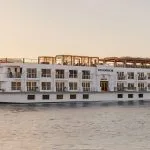 The elegant MS Jaz Senator Luxury Nile Cruise ship sailing on the Nile River at sunset, showcasing its multi-deck design and balconies.