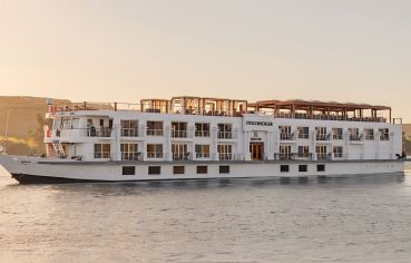 The elegant MS Jaz Senator Luxury Nile Cruise ship sailing on the Nile River at sunset, showcasing its multi-deck design and balconies.