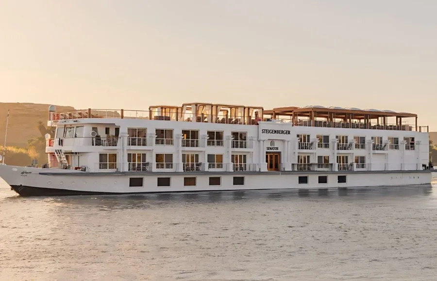 The elegant MS Jaz Senator Luxury Nile Cruise ship sailing on the Nile River at sunset, showcasing its multi-deck design and balconies.