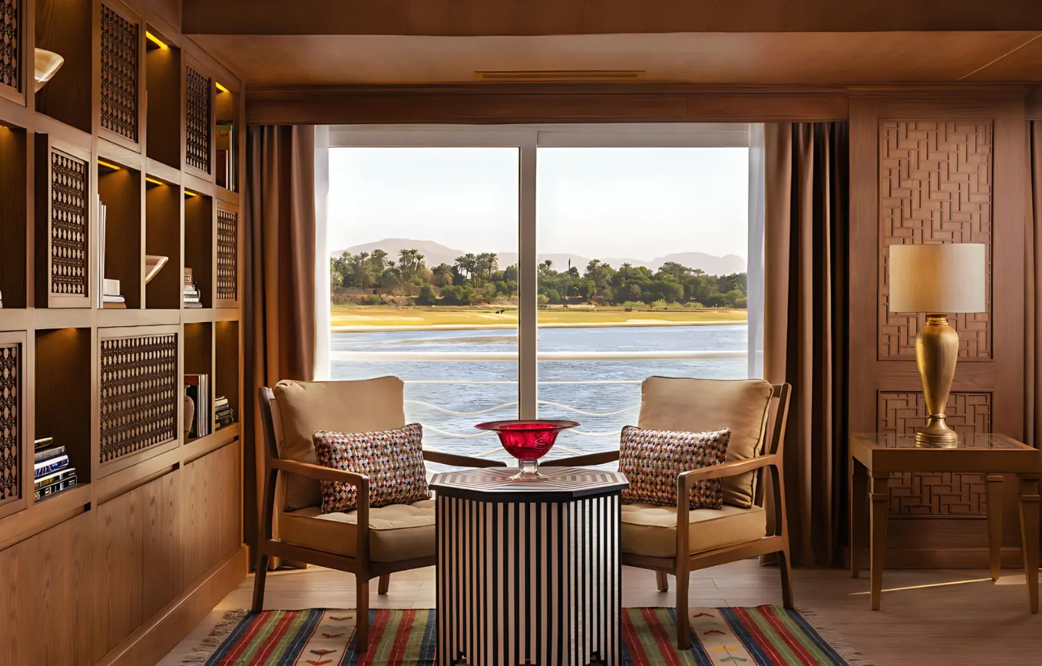 The elegant reading area of the Jaz Senator Nile Cruise, with two comfortable armchairs facing a large window with a scenic view of the Nile.