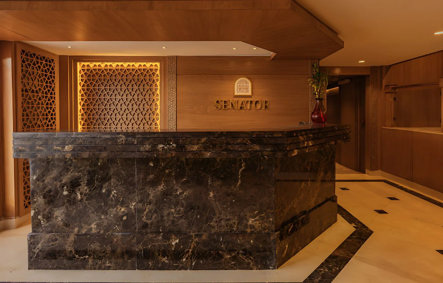 The elegant reception desk of the Jaz Senator Nile Cruise, featuring a dark marble countertop and intricate wooden decorative panels.