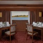 The elegant restaurant of the Jaz Senator Nile Cruise, with tables set for dining and large windows providing a view of the river and its banks.