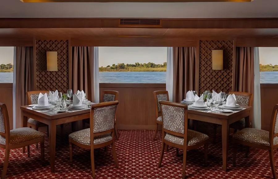 The elegant restaurant of the Jaz Senator Nile Cruise, with tables set for dining and large windows providing a view of the river and its banks.