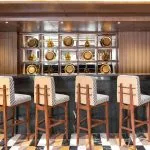 A modern and stylish bar on the Jaz Viceroy Cruise, with sleek bar stools and decorative gold plates on the shelves.