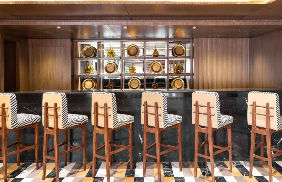 A modern and stylish bar on the Jaz Viceroy Cruise, with sleek bar stools and decorative gold plates on the shelves.