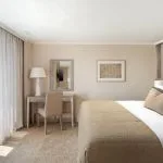 The elegant suite on the MS Jaz Viceroy Nile Cruise, featuring a comfortable bed, a dressing table, and a balcony with a view of the river.