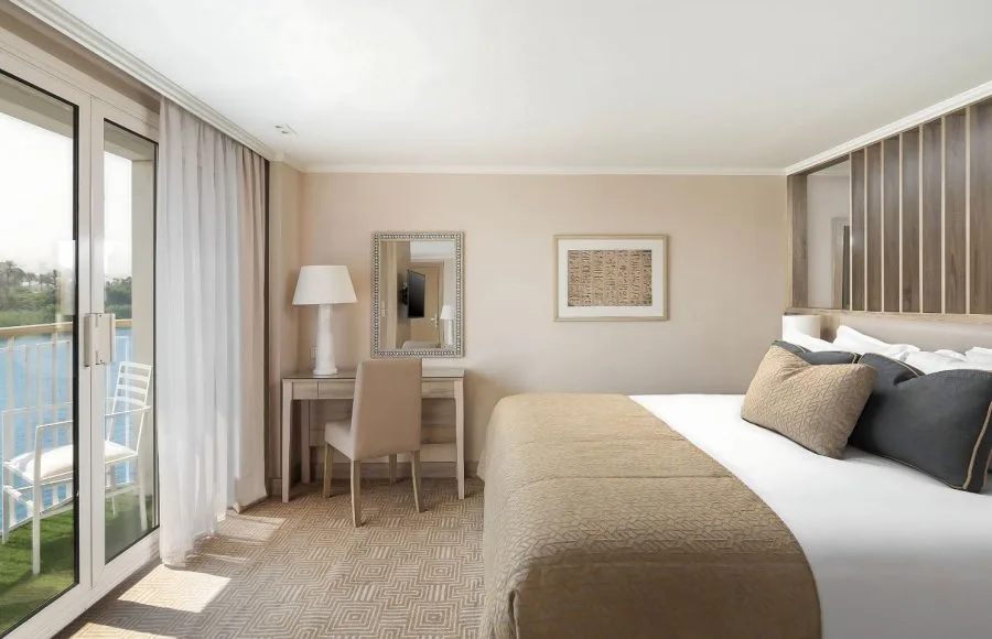 The elegant suite on the MS Jaz Viceroy Nile Cruise, featuring a comfortable bed, a dressing table, and a balcony with a view of the river.