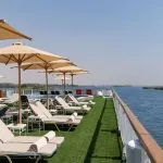 The sun deck of the Jaz Viceroy Cruise, showing a row of lounge chairs and umbrellas alongside the Nile River.