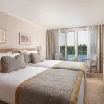 The elegant suite on the MS Jaz Viceroy Nile Cruise, featuring a comfortable bed, a dressing table, and a balcony with a view of the river.