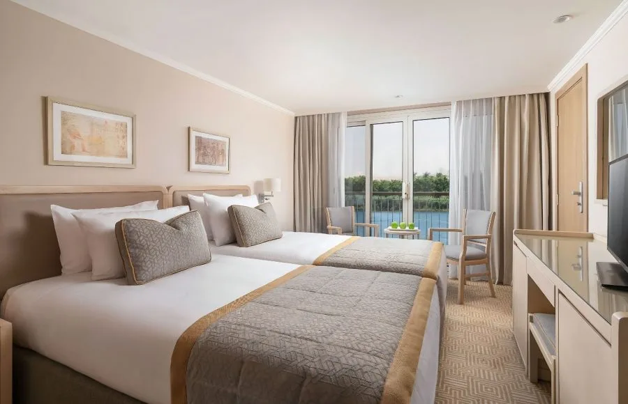 The elegant suite on the MS Jaz Viceroy Nile Cruise, featuring a comfortable bed, a dressing table, and a balcony with a view of the river.