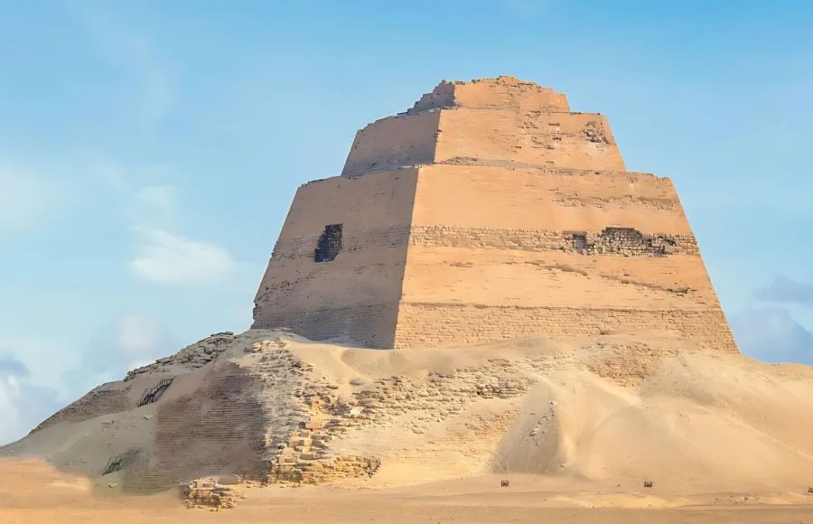 Ancient Meidum Pyramid ruins rising from desert sands under a clear sky.