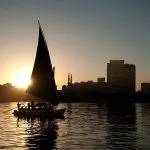 Silhouette of a felucca sailboat on the Nile River with the sun rising behind its sail.