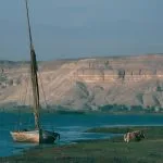 Nile felucca moored at Tel el-Amarna with desert cliffs towering in the background.