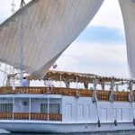 A large white Dahabiya sailing boat with two prominent lateen sails on the Nile River.