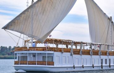 A large white Dahabiya sailing boat with two prominent lateen sails on the Nile River.