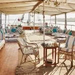Shaded upper sun deck with blue-and-white striped seating and wicker chairs.