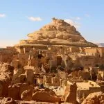 An imposing view of the ruined mud-brick fortress known as Old Shali, Siwa Oasis, built on a small rocky hill that dominates the surrounding structures in the desert.